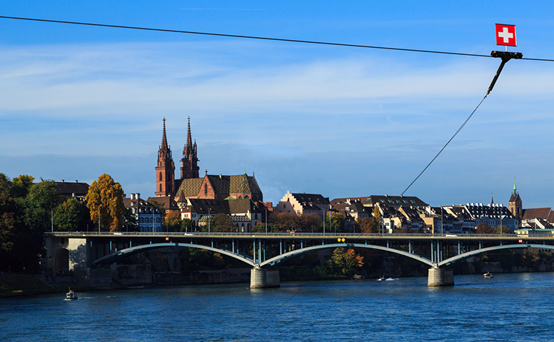 Switzerland: Panoramic view of the old town of Basel, looking across the River Rhine to a bridge, Swiss flag top right Switzerland: Panoramic view of the old town of Basel, looking across the River Rhine to a bridge, Swiss flag top right